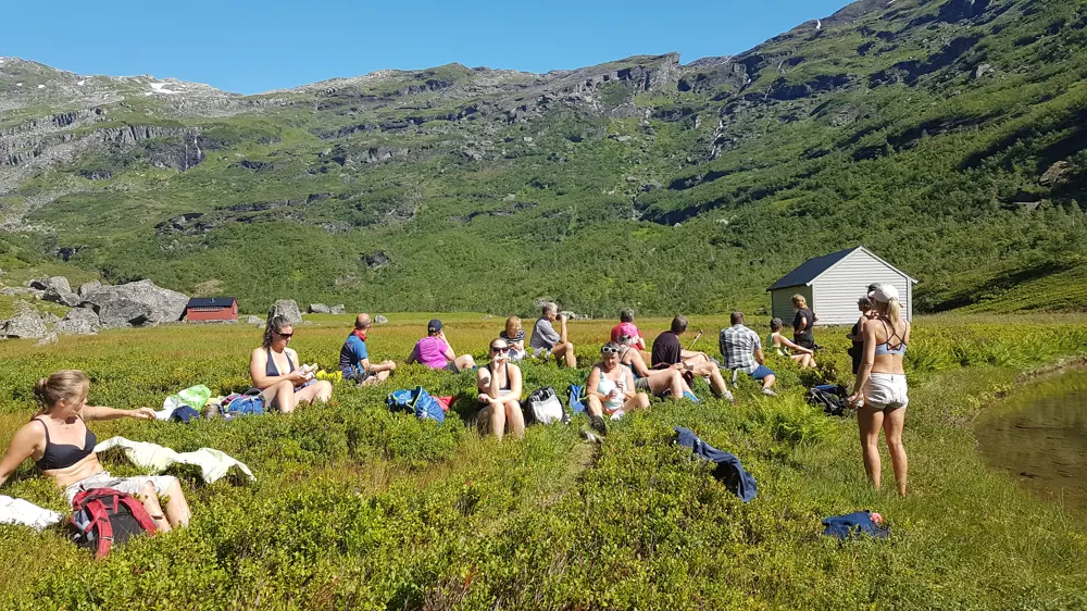 Folk som slappa av i lyngen, med fjell i bakgrunnen og blå himmel
