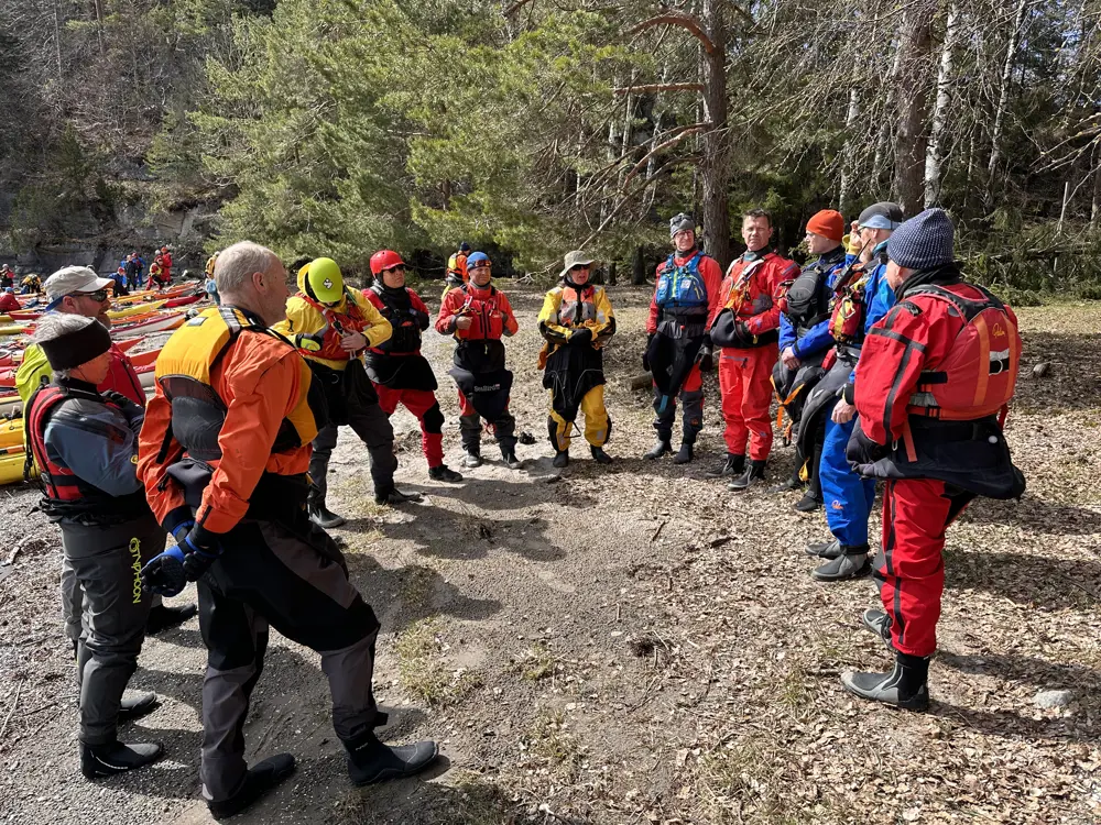 Bildet viser en rekke padlere på land, de står og lytter til en som prater.