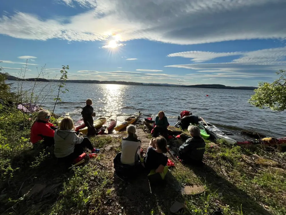 Bildet visere padlere i solnedgang. De er på land og har en pause.