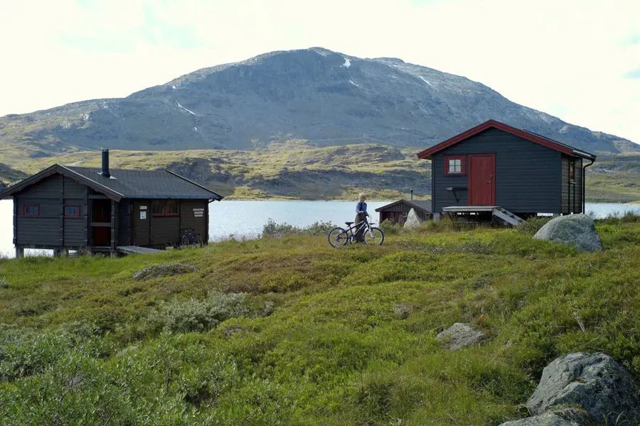 To hytter ved vann med fjell i bakgrunnen