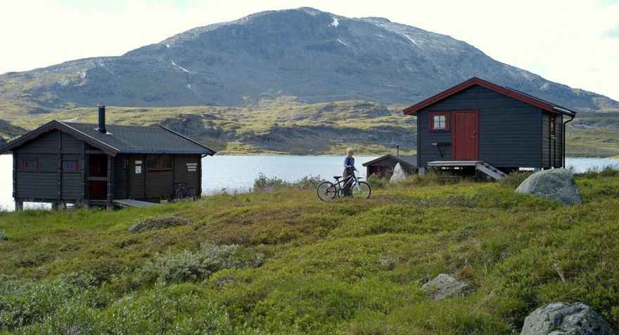 To hytter ved vann med fjell i bakgrunnen
