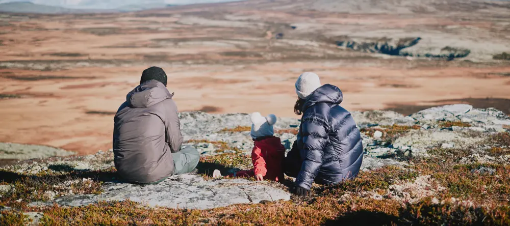 To voksne og et barn som sitter på en stein i fjellet. 