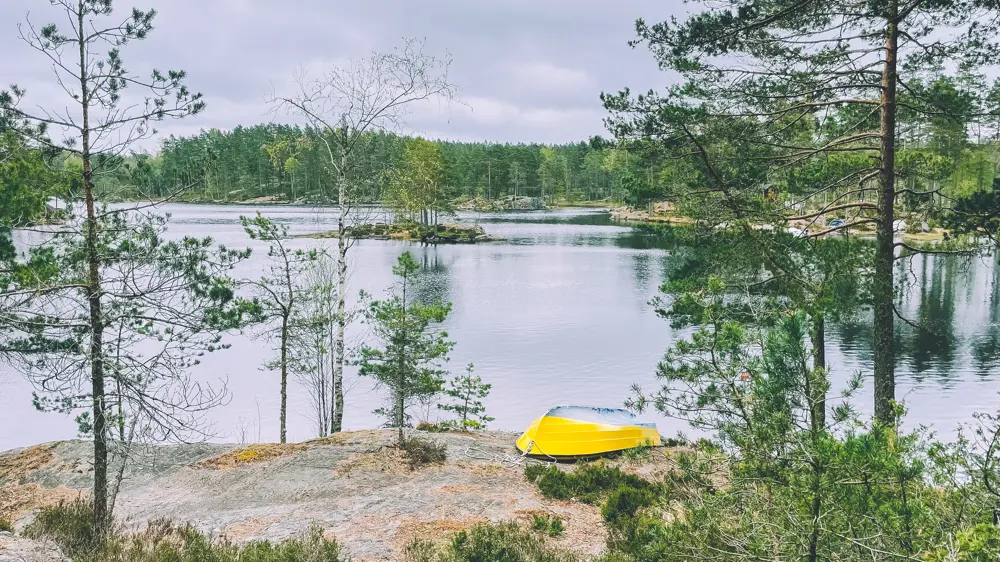 Gul båt på berg med vann og skog i bakgrunnen.