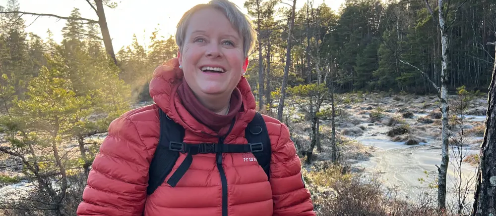 Smilende kvinne på tur i skogen. Foto.