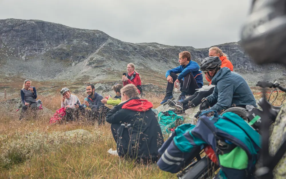En gruppe ungdommer som har matpause, sitter på steiner i fjellet, som sykler Rallarvegen