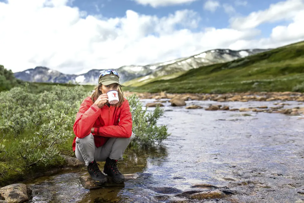 Dame drikker vann fra fjellbekk