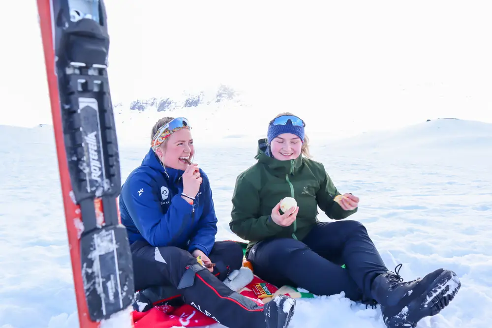 To damer sitter i snøen og spiser appelsin