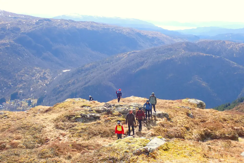 En gruppe mennesker går tur på sti, med fjell og himmel bak i bildet