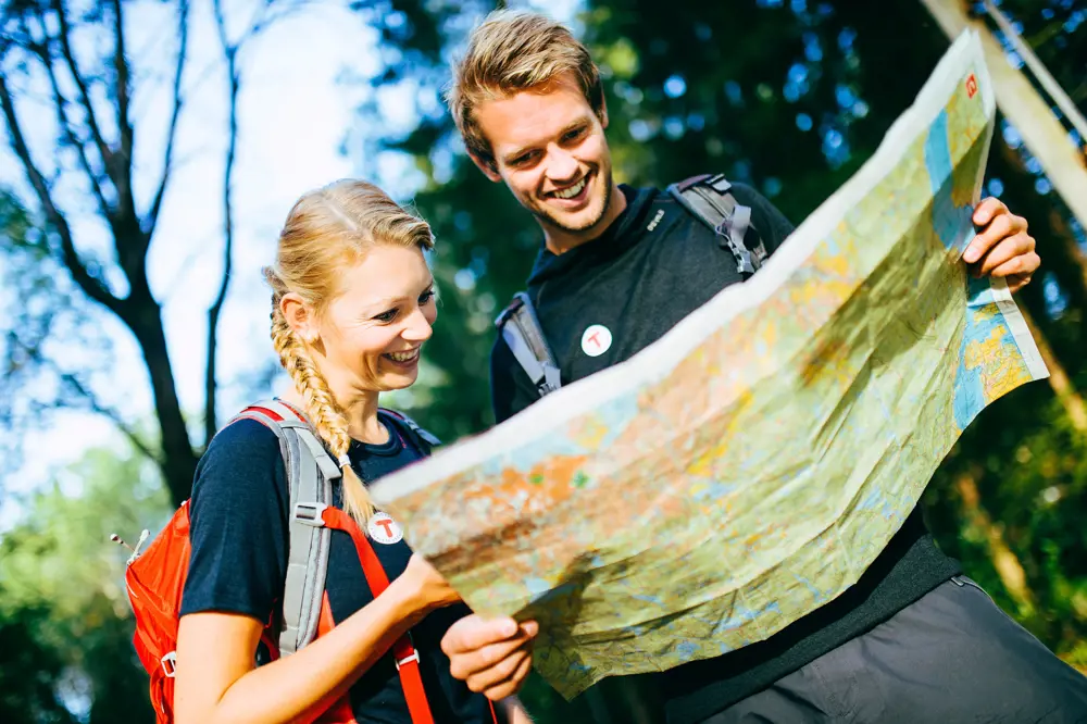 En mann og en dame som står i skogen og titter ned i et stor kart.