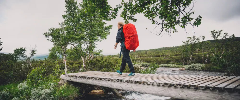 Dame med tursekk som går over en bro