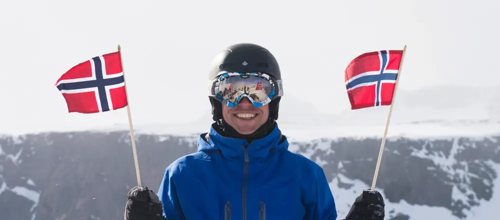 Flagging på Rasletind, en smilende fyr med skibriller og et norsk flagg i hver hånd.