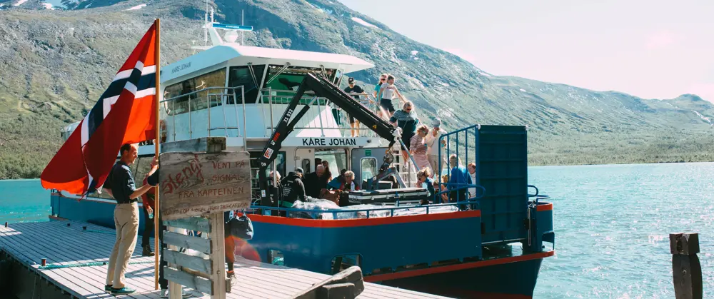 Norsk flagg og båten på Gjende, som glitrer i solen. 