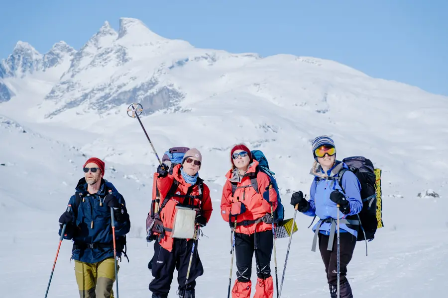 Gruppe på ski blant snøkledde fjell.