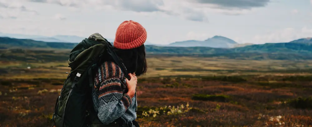 Person med sekk og oransje lue som ser utover fjellet