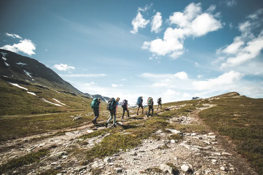 Bildet viser en gruppe mennesker på rekke og rad langs en sti i fjellet i fint sommervær.
