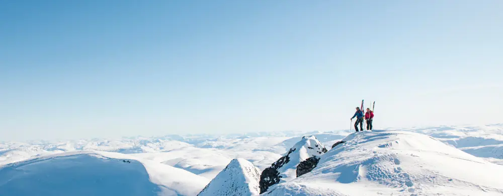 To personer med ski på sekken på en snødekket fjelltopp