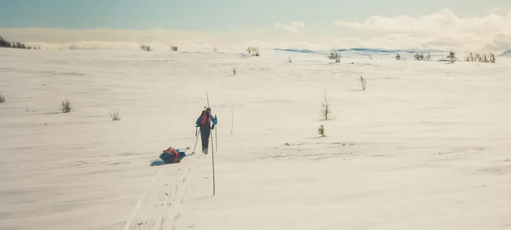 Mann med fjell og pulk som går langs en kvistet løype