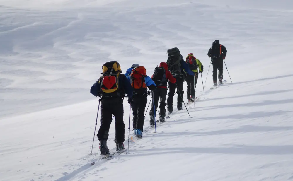 Toppturgåere i tog oppover gjennom snødekt landskap.