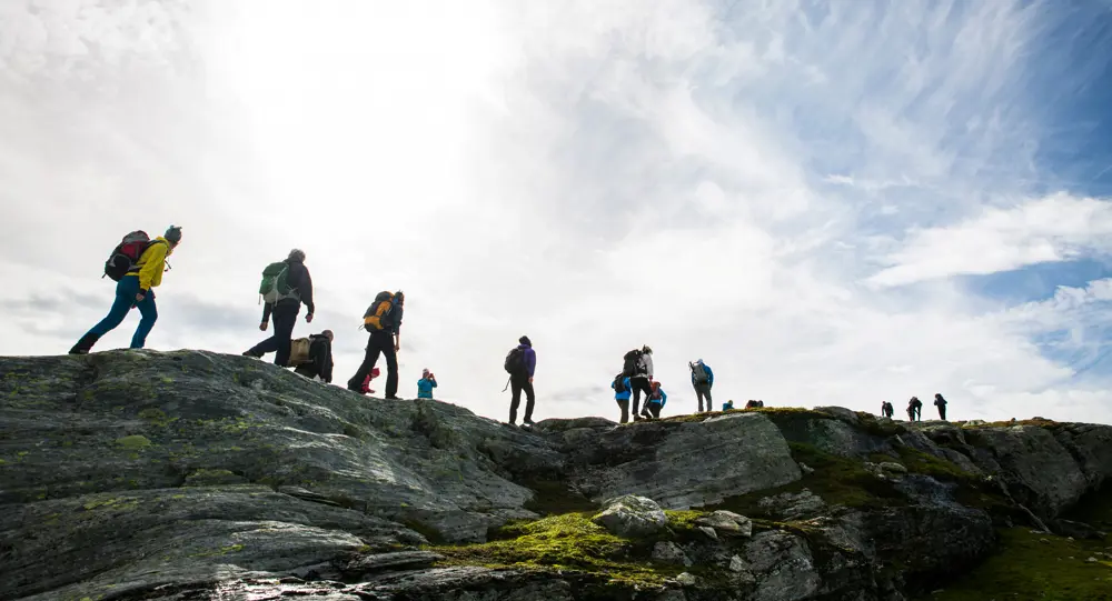 Mennesket på tur over en fjellrygg. Lettskyet og motlys. Foto