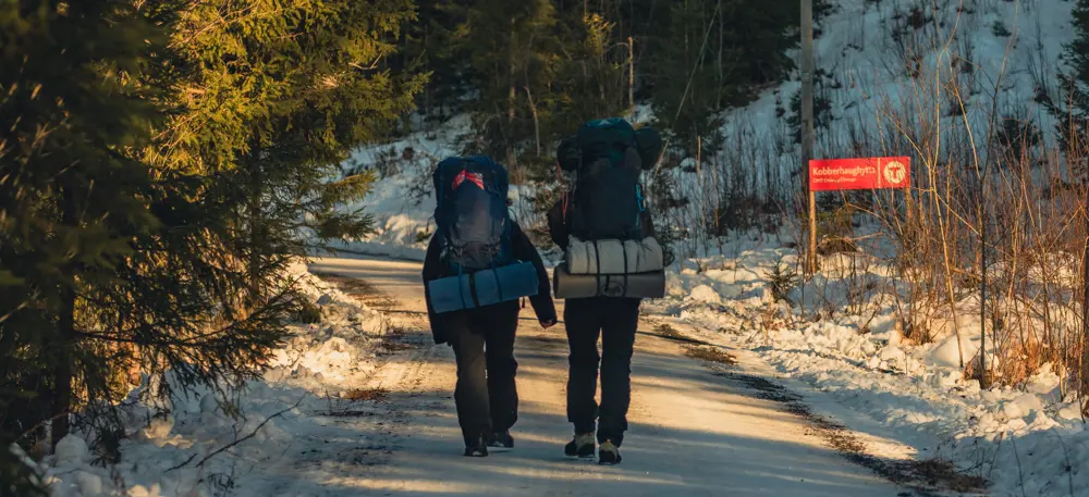 To personer med sekk som går tur på en grusvei dekket av snø