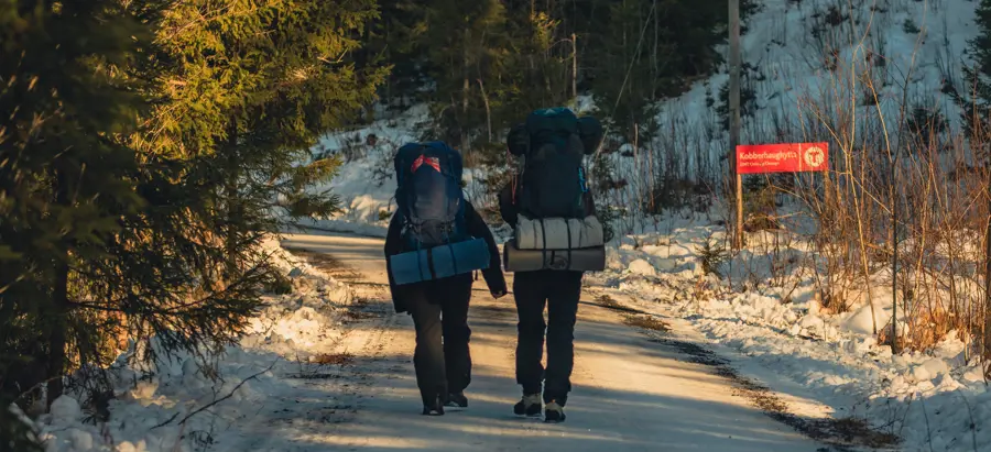 To personer med sekk som går tur på en grusvei dekket av snø