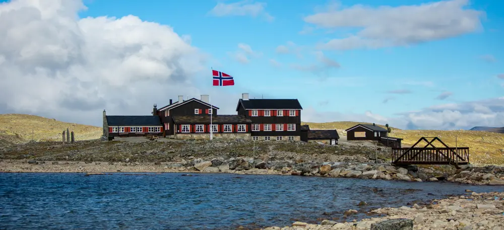 Svartmalt hytte med rød karmer og en flaggstang med norsk flagg foran hytta