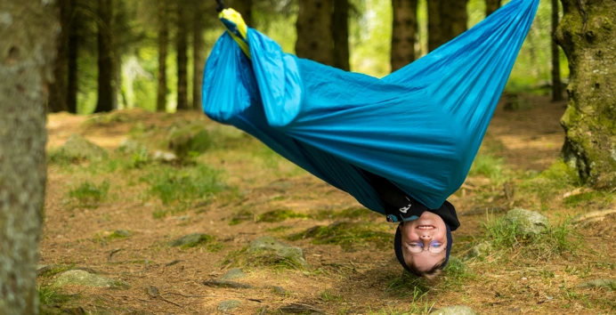 En gutt henger opp ned i hengekøye.