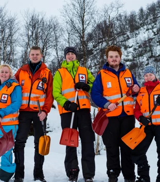 Fem personer med oransje vester og hver sin spade står i snøen og smiler