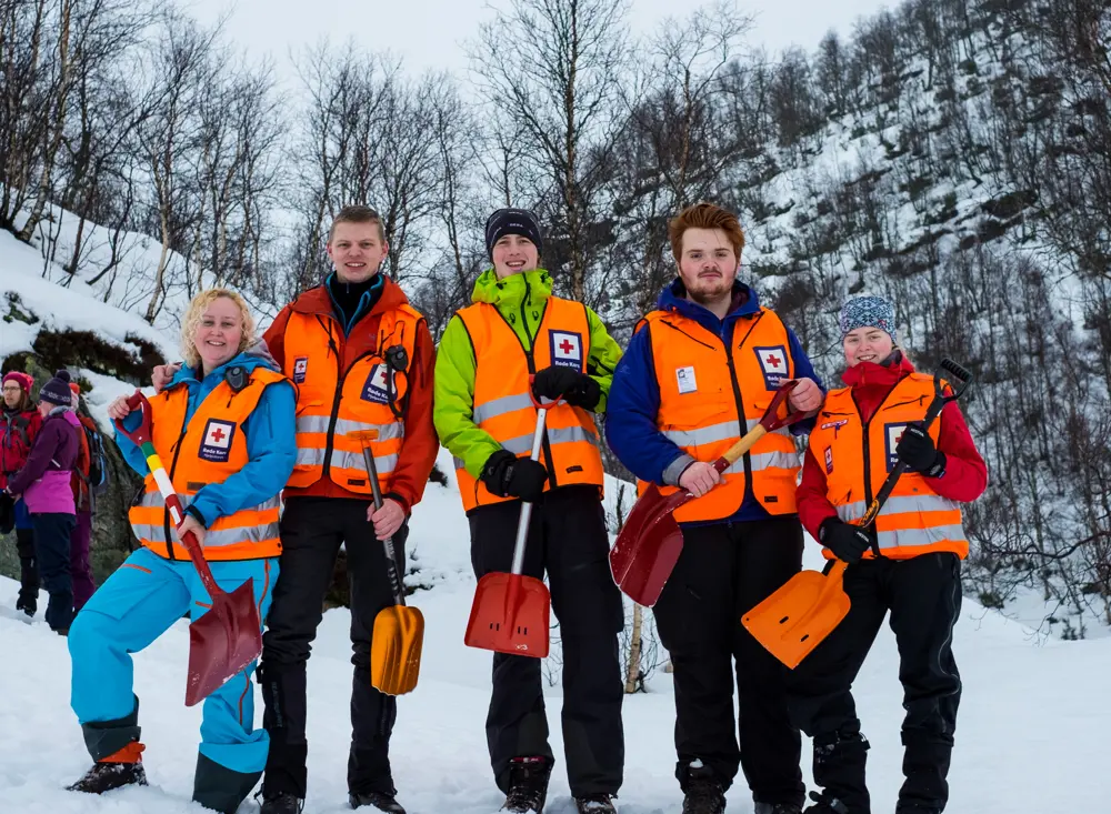 Fem personer med oransje vester og hver sin spade står i snøen og smiler