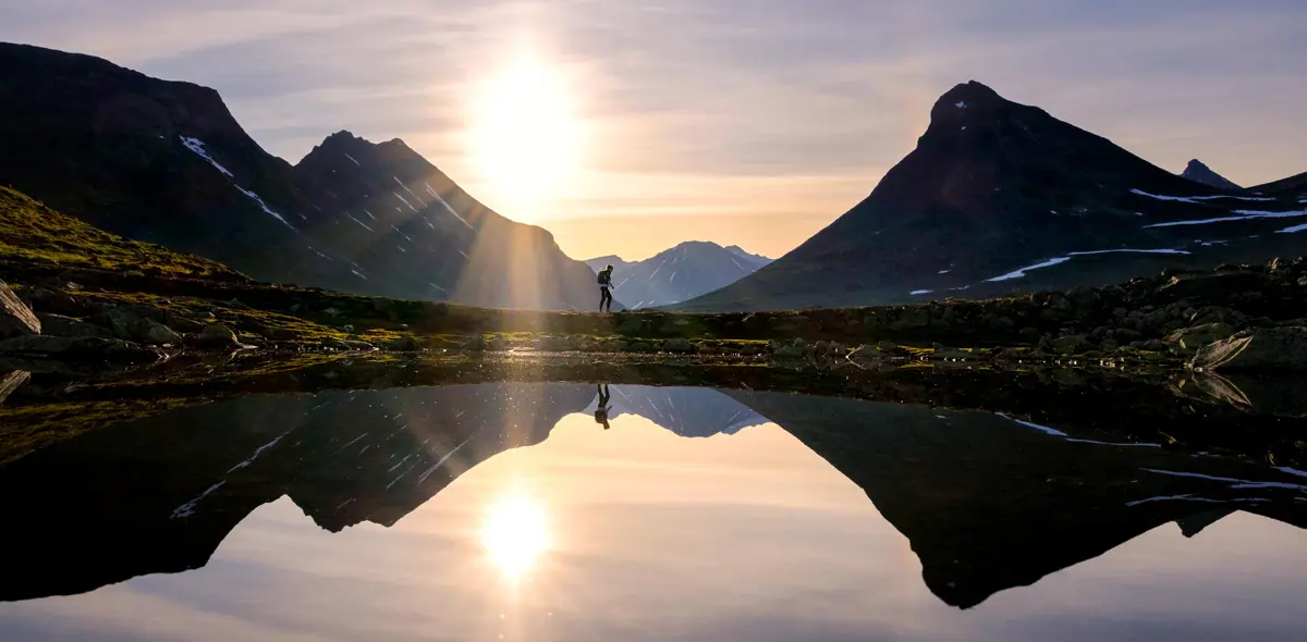 Vann, fjell og turgåere i solnedgang