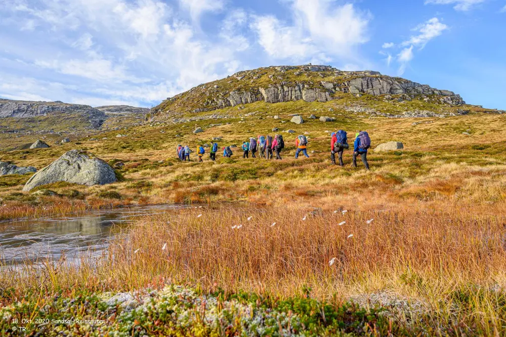 En gruppe med mennesker som går innover fjellheimen med tursekk