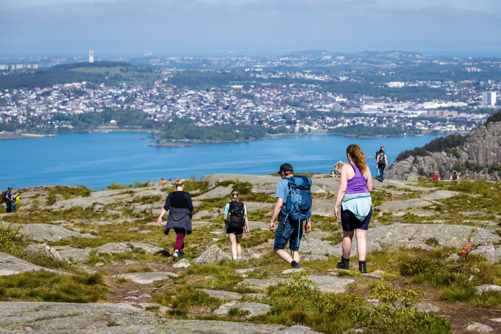 Fire voksne er på tur ned fra et fjell. Sjø og by i bakgrunn