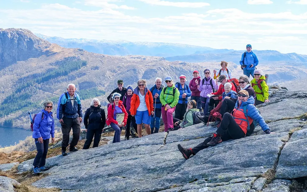 En stor turgruppe med mennesker i fargerike klær som er avbildet på en topptur i fjellet.