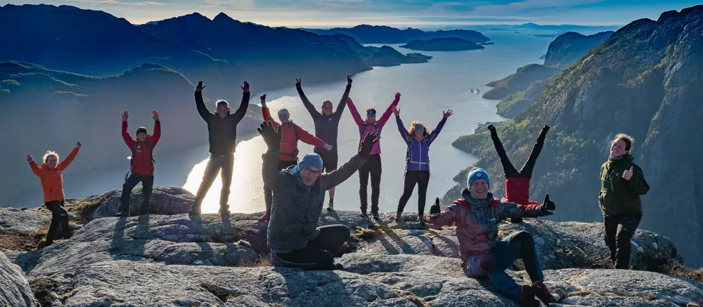 Mennesker på en fjelltopp som rekker hendene i været.