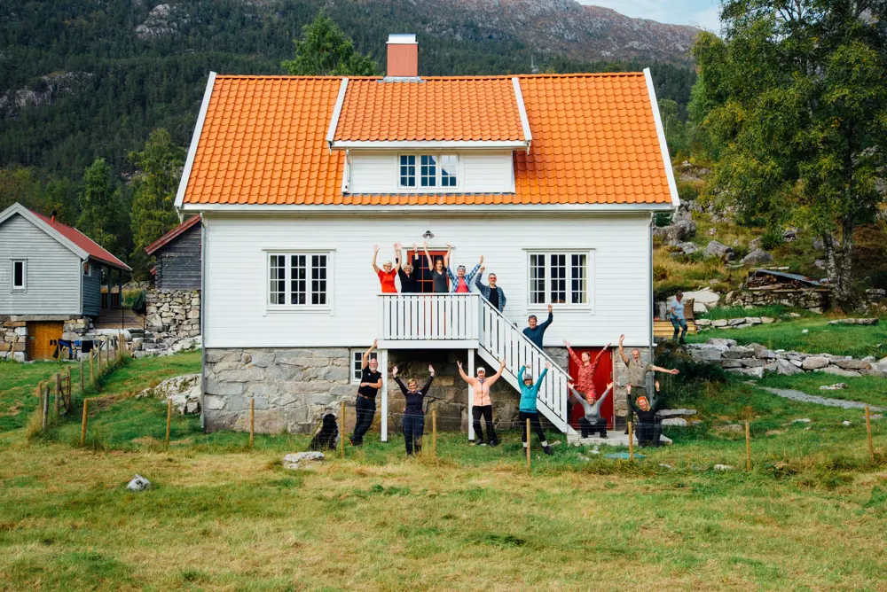 Flere mennesker står foran et hvitt hus og holder hendene i været.