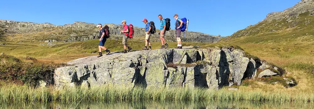Fem personer som går over et berg, speilbilde i vannet nedenfor.