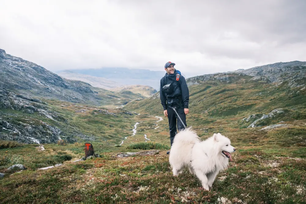 Mann med svarte turklær og caps står sammen med stor hvit hund på fjellet