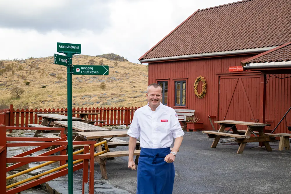 Bilde av bestyreren av Gramstadtunet som går fra friluftslåven og mot kamera. Han er kledd i hvite kokkeklær.
