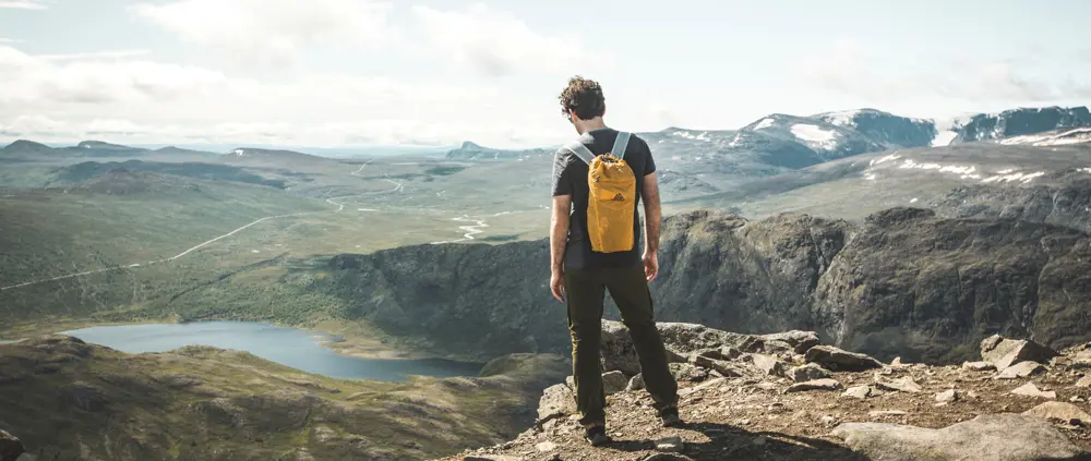 Person står med sekk på ryggen og ser utover vakkert fjellområde