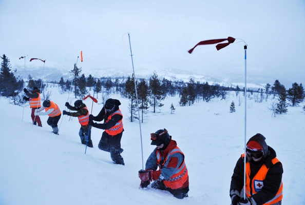 Flere personer i oransje vester graver i snøen.