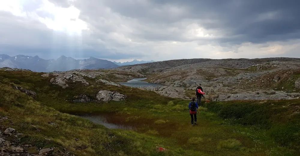 To turgåere går over svabergområde. Flotte fjell i bakgrunnen.
