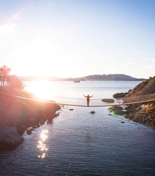 Dronebilde av hengebru på Vassøy i Stavanger. En person står i midten av broen og strekker armene ut.