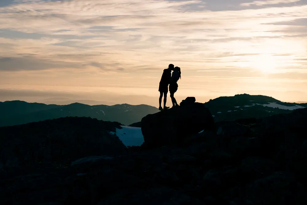 Kjærestepar kysser i solnedgang på fjelltopp.