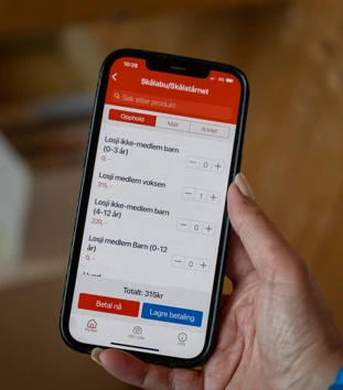 Mobiltelefon i hånden med ulike hyttekategorier.