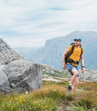 En mann i gul t-skjorte og shorts går på toppen av et fjell.