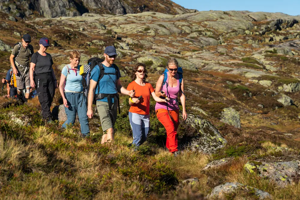 En gruppe mennesker går nedover en fjellside. Kvinnen som går i front blir støttet av ledsagere.