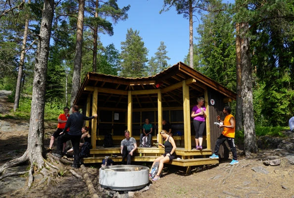 Gapahuk i skogen med sitteplasser og bålpanne.