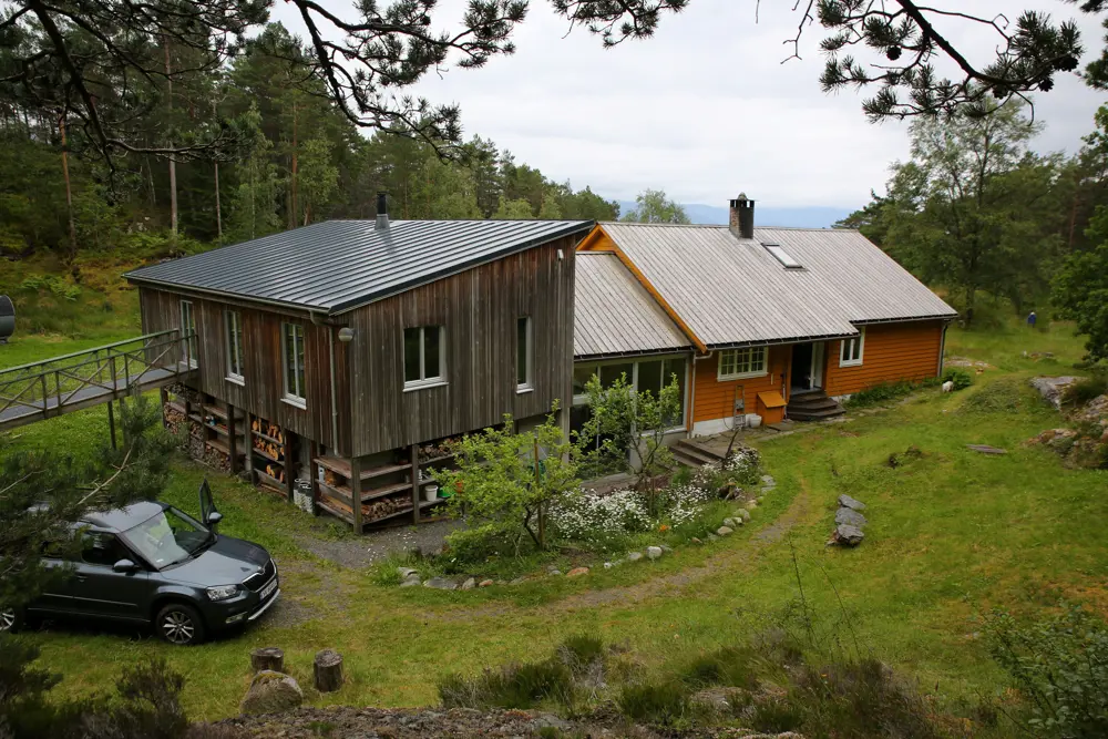 Okerfarget og grå, stor hytte som ligger ved skog og stor plen.