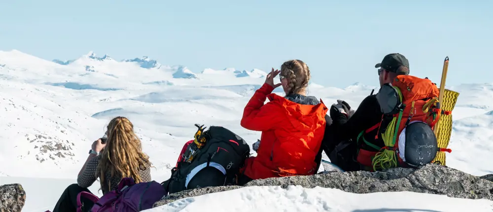 Tre personer som speider utover snødekte fjell