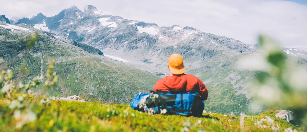 Mann med caps og rød jakke som ser utover fjellet.